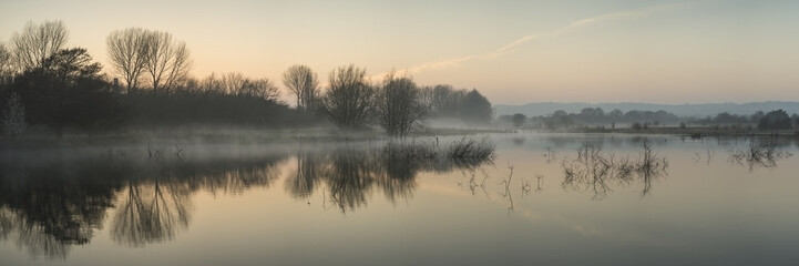 Wall Mural - panorama landscape of lake in mist with sun glow at sunrise