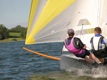 Two People Sailing A Small Grey Dinghy On A Lake