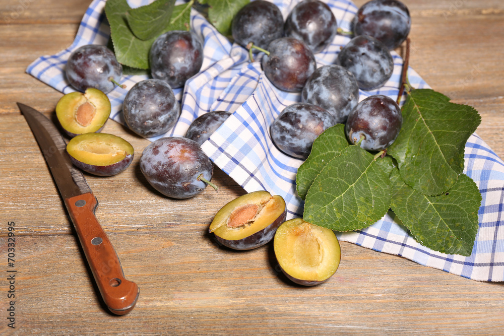 Ripe sweet plums with leaves, on wooden table
