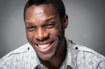 Laughing black man close up portrait against grey background.