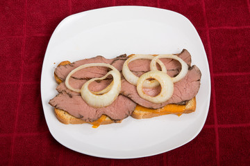 Wall Mural - Hot Sliced Beef Sandwich with Onion Rings on Red Table