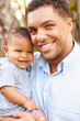 © Monkey Business - Portrait Of Smiling Father Holding Baby Son Outdoors