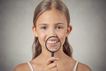 girl showing teeth through a magnifying glass grey background  