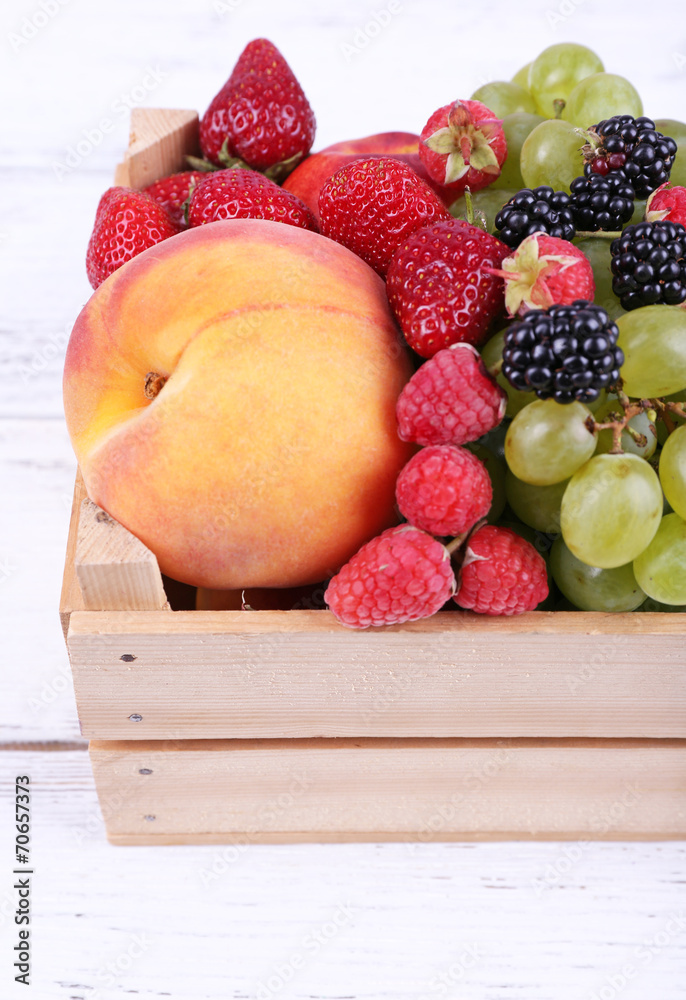 Different berries and fruits in box on wooden table close-up