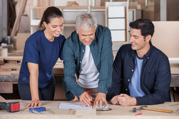 Carpenter Drawing Blueprint With Team At Table