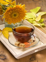 Wall Mural - glass cup with tea on a tray with autumn leaves and flowers