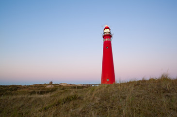 Fototapete - red lighthouse at sunset on island coast