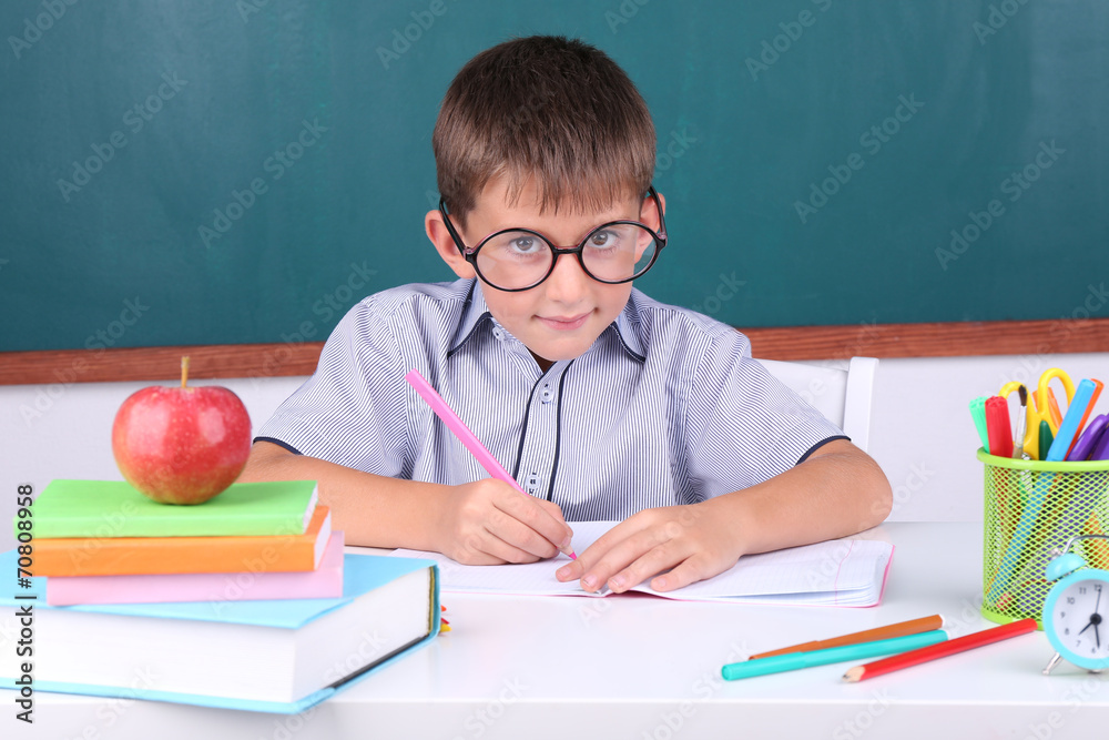 Schoolboy sitting in classroom on blackboard background