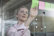 © Westend61 - Germany, Munich, Businesswoman in office, putting sticky notes on glass pane