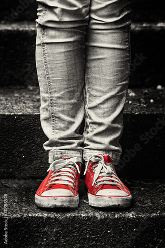 Naklejka na szybę Little girl in red sneakers and jeans standing on the stairs