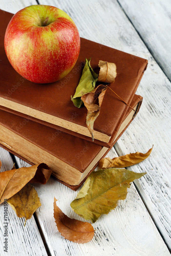 Apple with books and dry leaves on wooden background