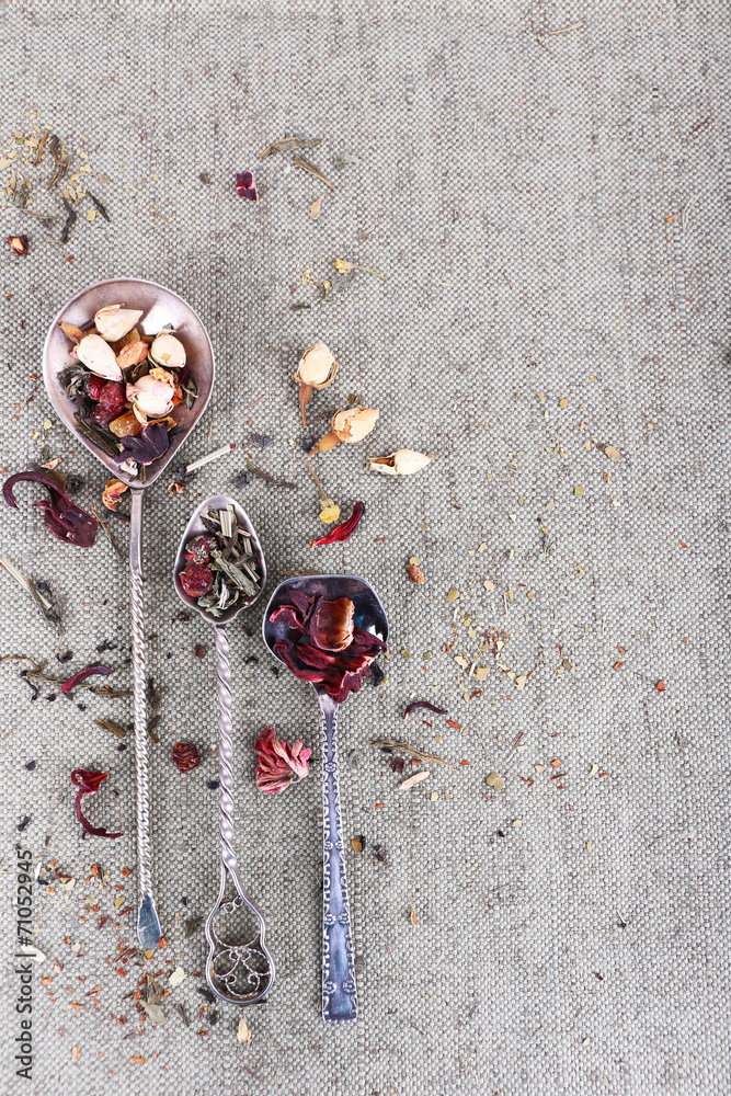 Tea in metal spoons on grey fabric background
