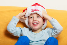 Little Boy In Red Santa Hat Sitting On Couch At Home