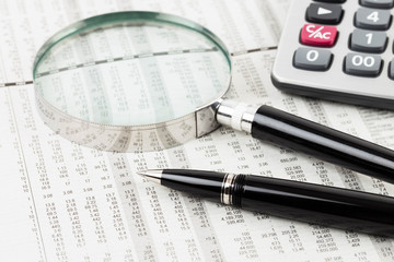 pen, calculator, and magnifier rest on stock price detail financ