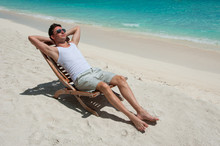 Man In Chair Sunbathing On The Beach Near The Sea