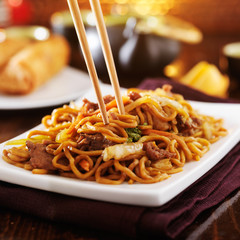 eating chinese beef lo mein with chopsticks