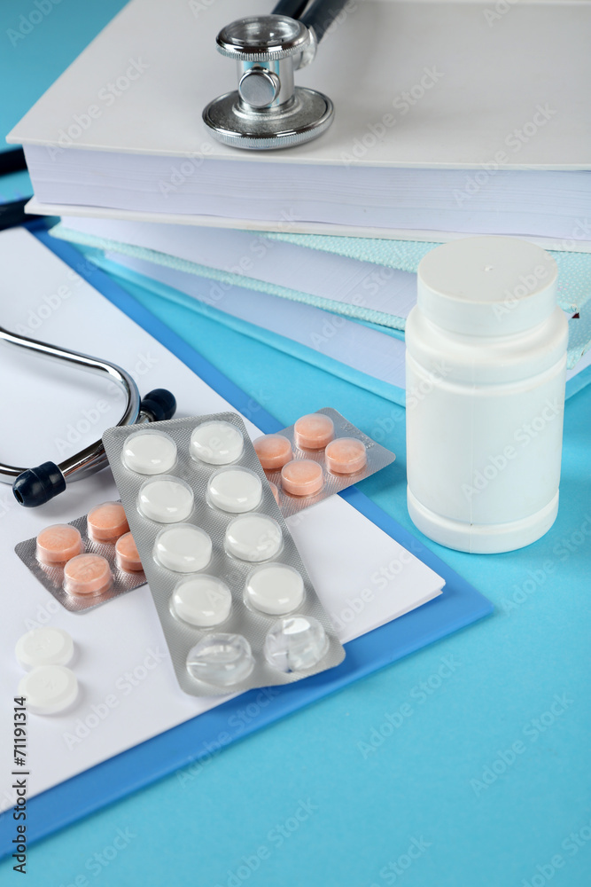 Medical stethoscope with books and tablet on blue background
