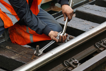 Worker tightens the screw on railroad with two spanners in hands