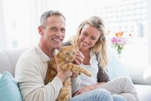 Smiling Couple Petting Their Gringer Cat On The Couch