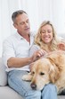 © WavebreakMediaMicro - Smiling couple petting their golden retriever on the couch