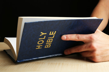 Wall Mural - Male hands with Bible on wooden table on dark background