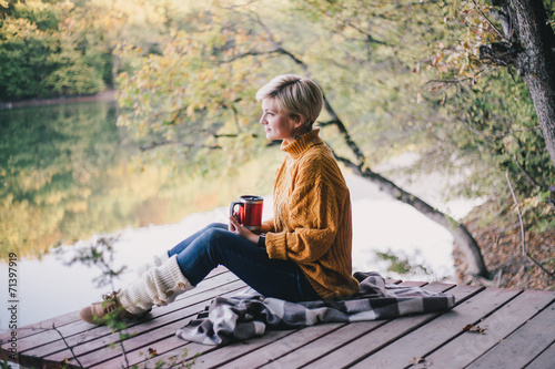Fotografía Blond with blue eyes sitting near lake with cup of hot tea