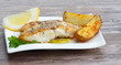 White fish with potato wedges on white plat, wooden background
