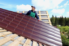 Worker Puts The Metal Tiles On The Roof Of A Wooden House