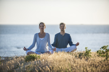 handsome couple practicing meditation exercises on the beach at