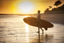 Silhouette Of A Man With His Paddle Board On The Beach At Sunset