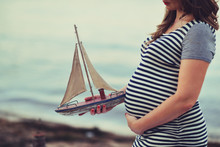 On Sea Background Pregnant Woman's Belly And Hand Model Sailboat