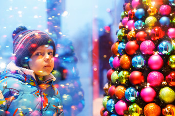 Adorable little boy looking through the window at Christmas deco