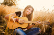 beautiful girl playing the guitar in a wheat field