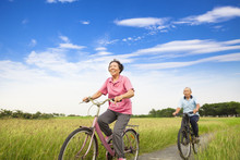 Happy Asian Elderly Seniors Couple Biking In Farm