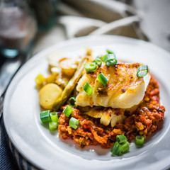 Wall Mural - Roasted hake with romesco sauce and onion on wooden background