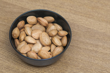 Almonds on a black bowl on wooden background