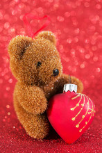 Xmas Decor Cute Bear With Glass Heart. Christmas Decoration On Red Glitter Blur Background