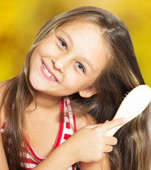 Wall Mural - smiling little girl brushing her hair on a golden background