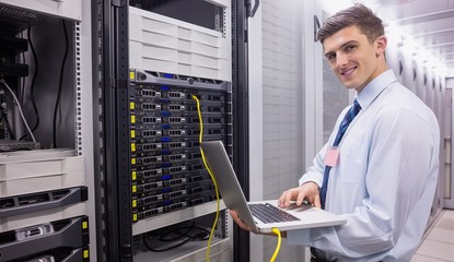 Wall Mural - Smiling technician using laptop while analysing server