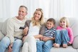 © WavebreakmediaMicro - Smiling family sitting on sofa changing tv channel