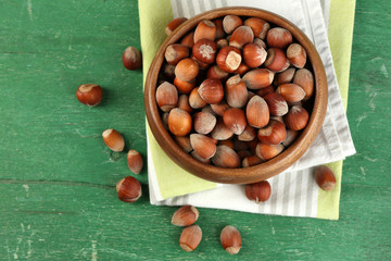 Hazelnuts in wooden bowl, on napkin on wooden background