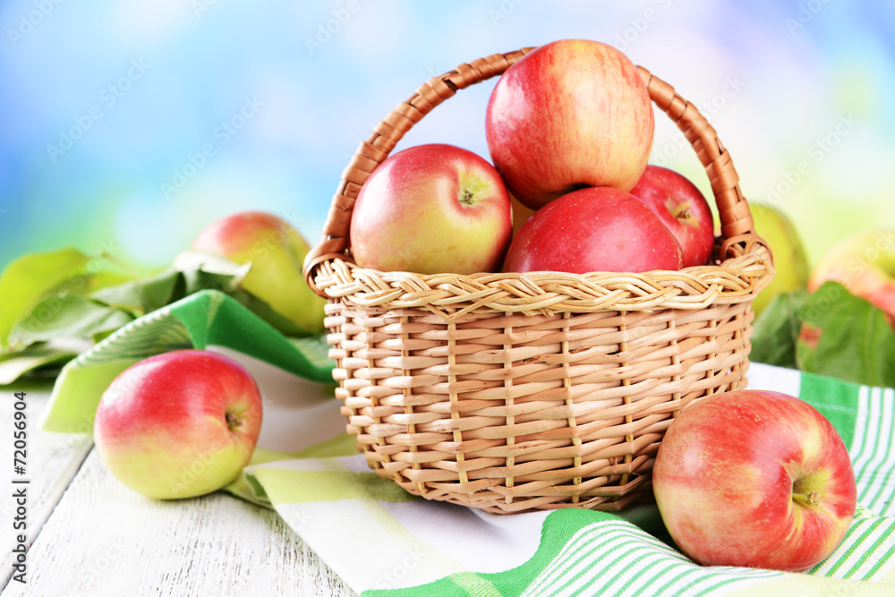 Sweet apples in wicker basket on table on bright background