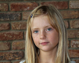 a young girl looking pensive, with a brick wall background