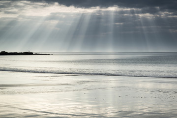 Wall Mural - Stunning sun rays bursting from sky over empty yellow sand beach