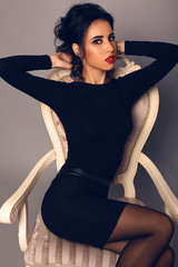sexy girl with dark hair in elegant black dress posing at studio