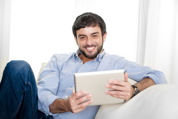 Young attractive Hispanic man on couch with digital tablet pad