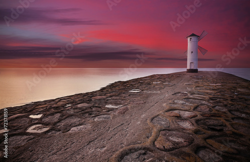 Fototapeta na wymiar Lighthouse windmill with dramatic sunset sky.