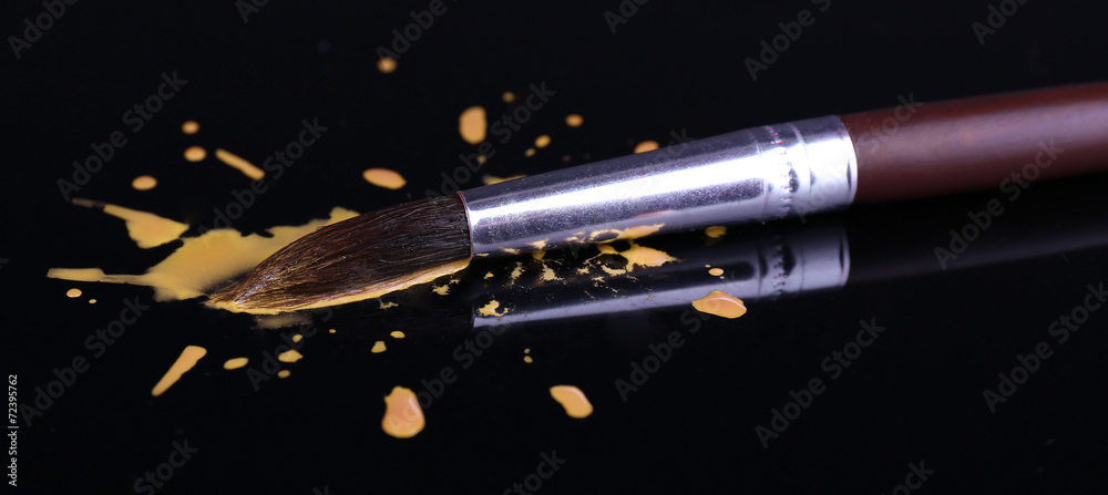 Spilled paint and brush isolated on black