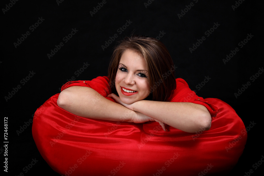 Uśmiechnięta dziewczyna na czerwonej poduszce. - obrazy, fototapety, plakaty 