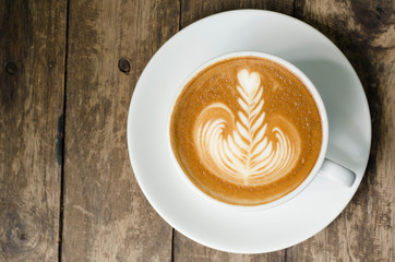 White cup of latte art coffee on grained wood top view